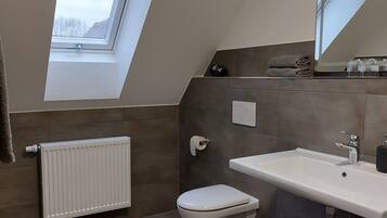 A modern bathroom with a skylight, a toilet, a sink, and a radiator.