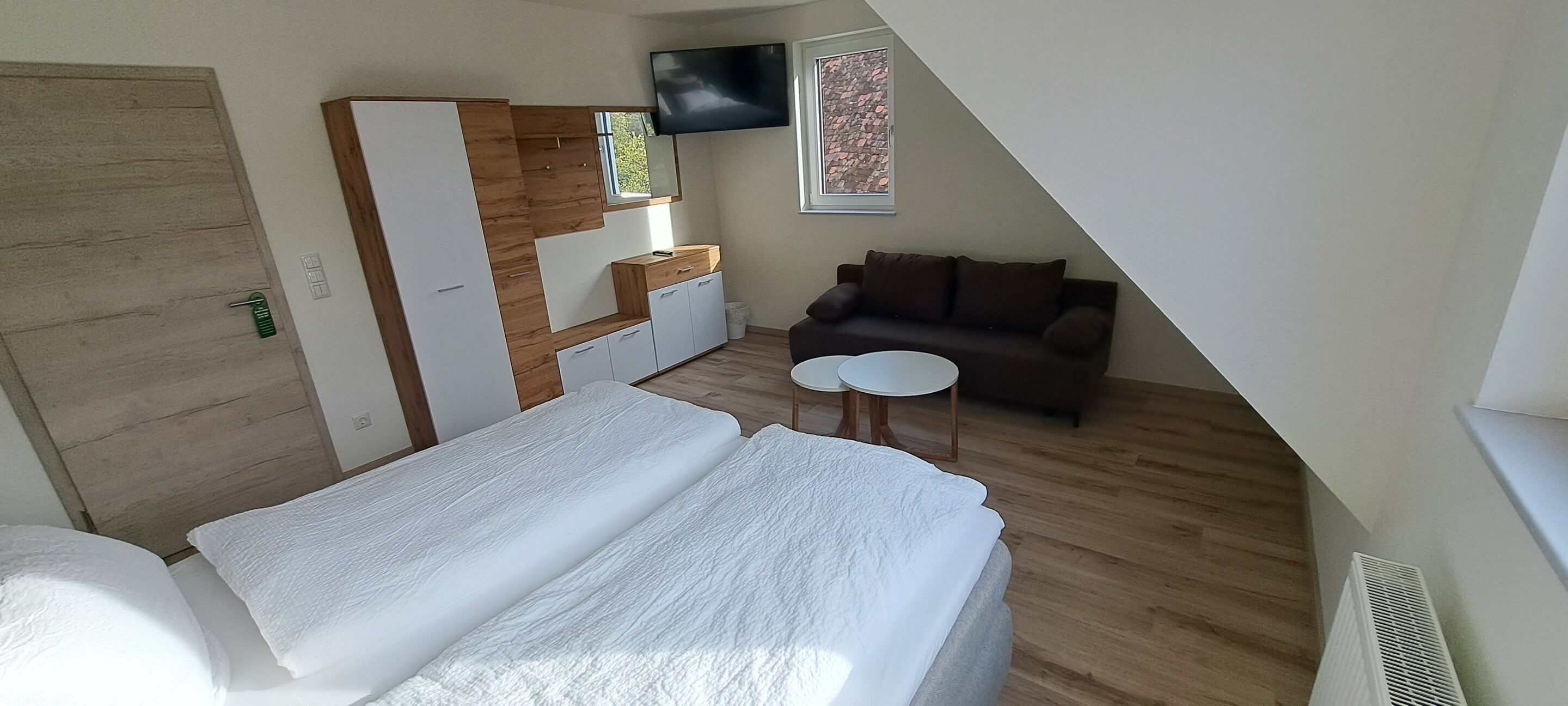 Un dormitorio con cama, una mesita pequeña, sofá, televisor y ventana.
