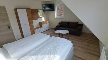 Un dormitorio con cama, una mesita pequeña, sofá, televisor y ventana.