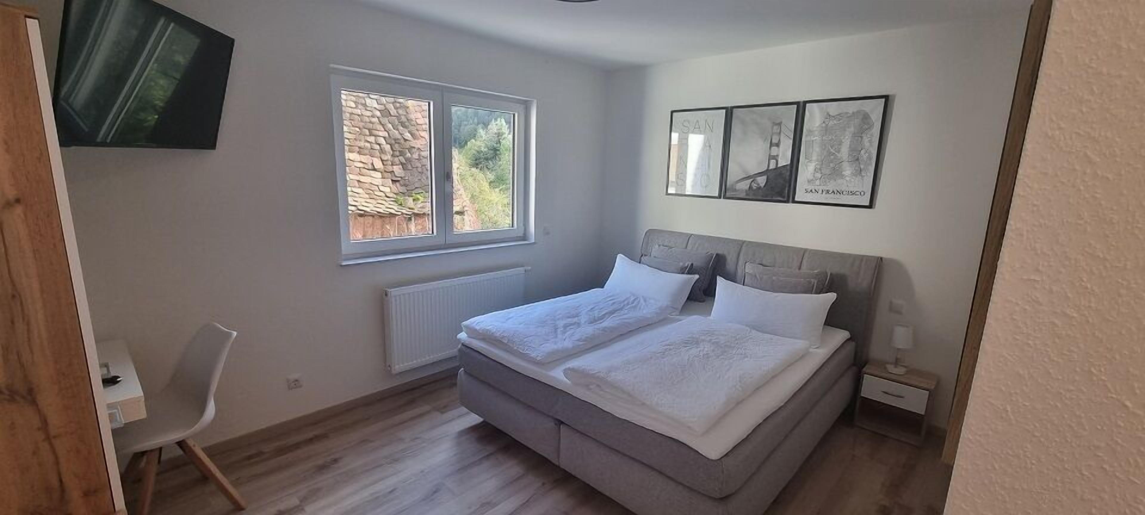 Ein Schlafzimmer mit einem Bett, einem Sessel, einem Fenster und Bildern an der Wand.