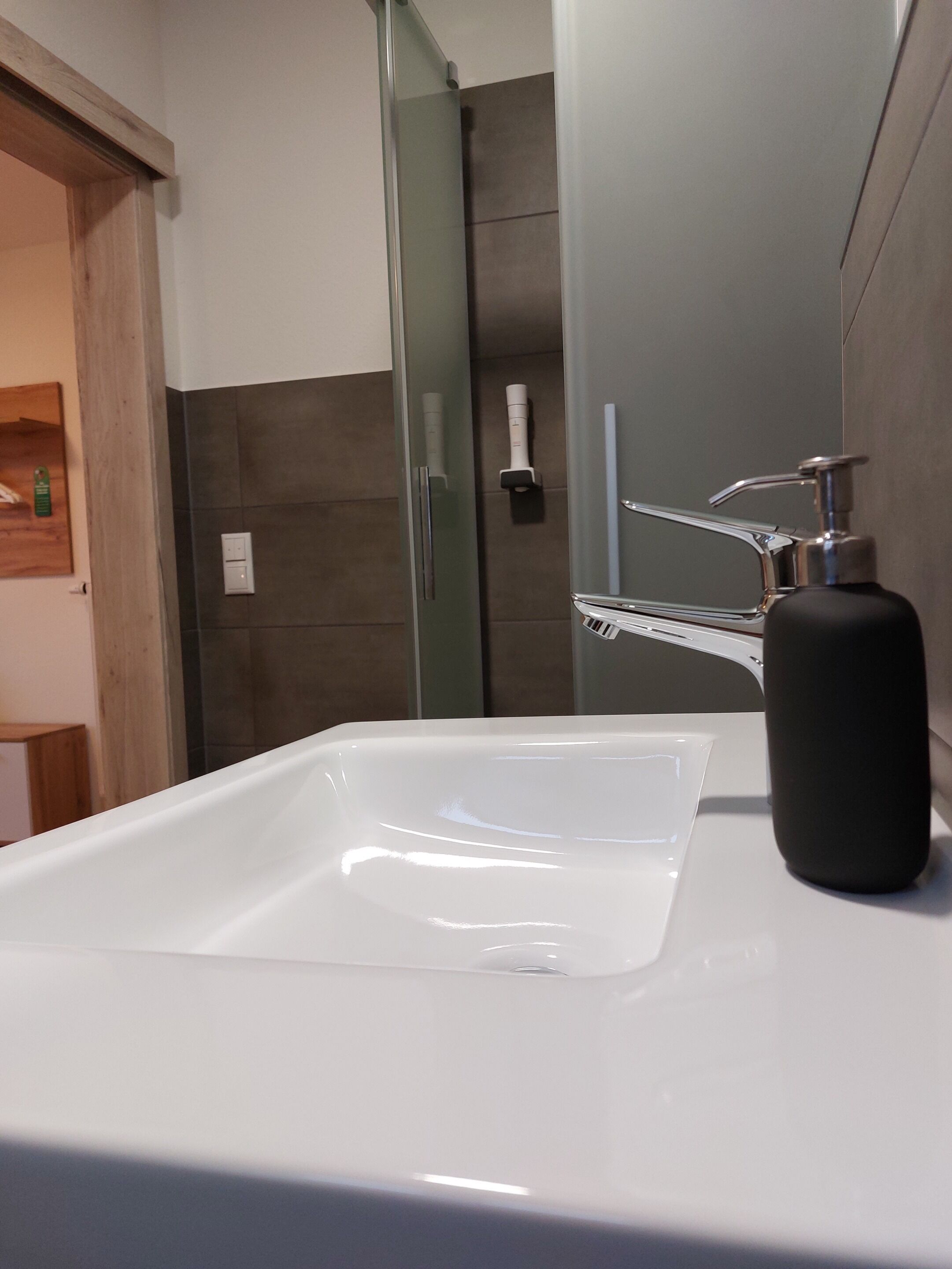 A bathroom with a white sink, a black soap dispenser, and a glass shower enclosure.