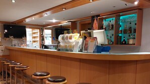 Zona de bar con taburetes, mostrador y estanterías llenas de botellas.