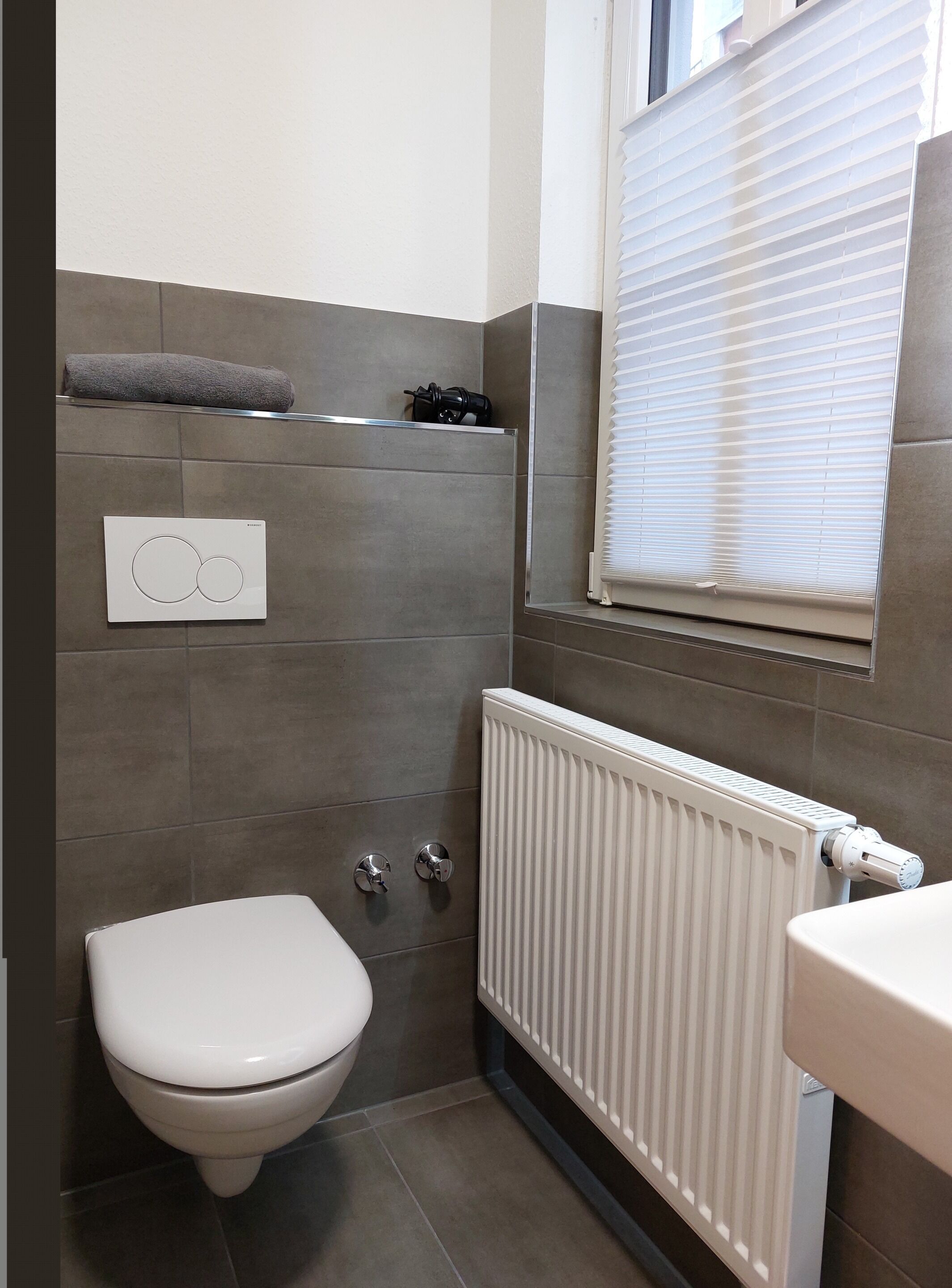Un bagno moderno e piccolo, con il water, un termosifone e una finestra con persiane.