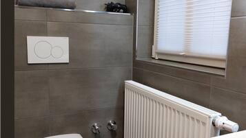 Un bagno moderno e piccolo, con il water, un termosifone e una finestra con persiane.