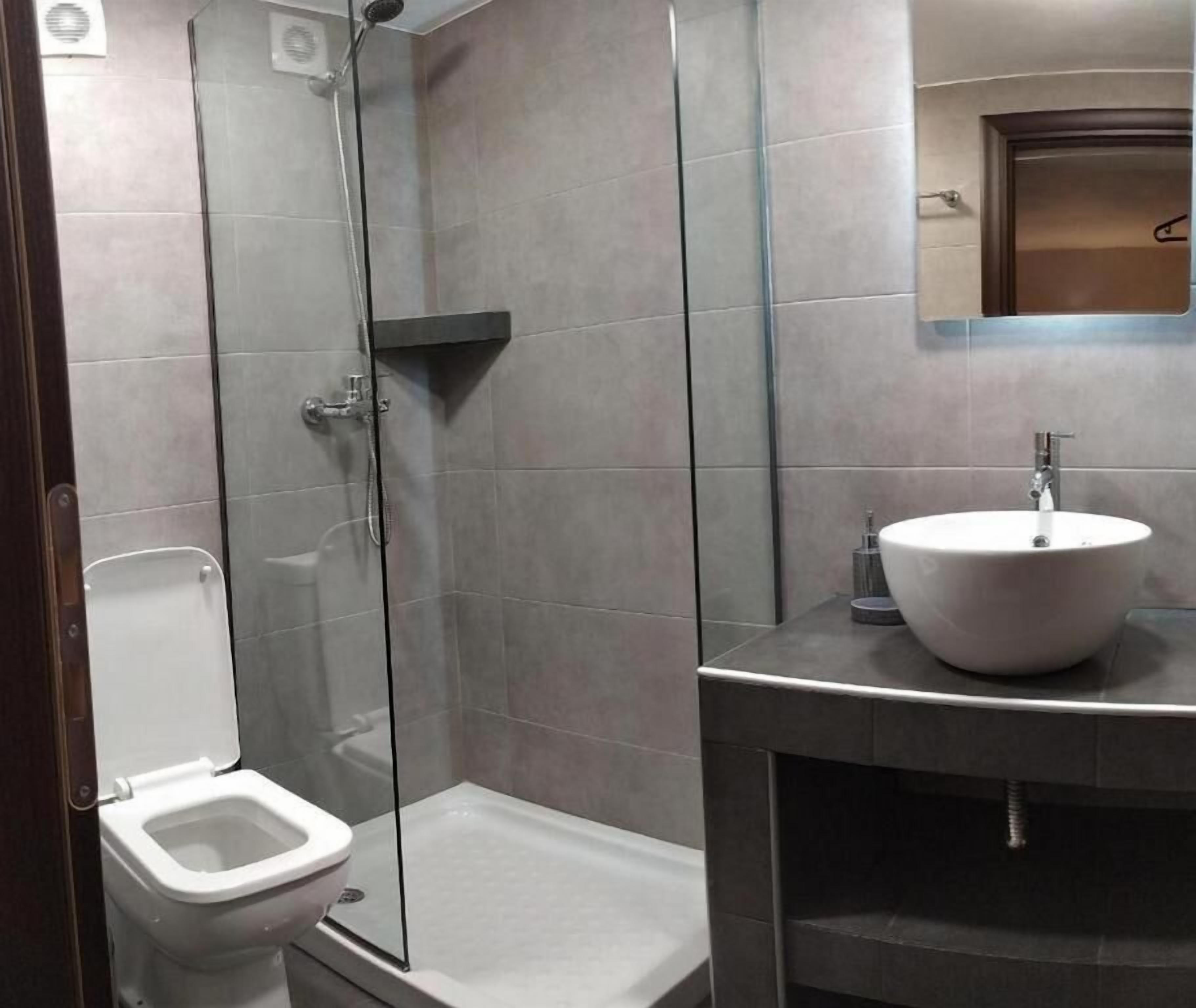 Ein modernes Badezimmer mit einer Glaskabine zur Dusche, einer weißen Toilette und einem großen Waschbecken mit Spiegel darüber.