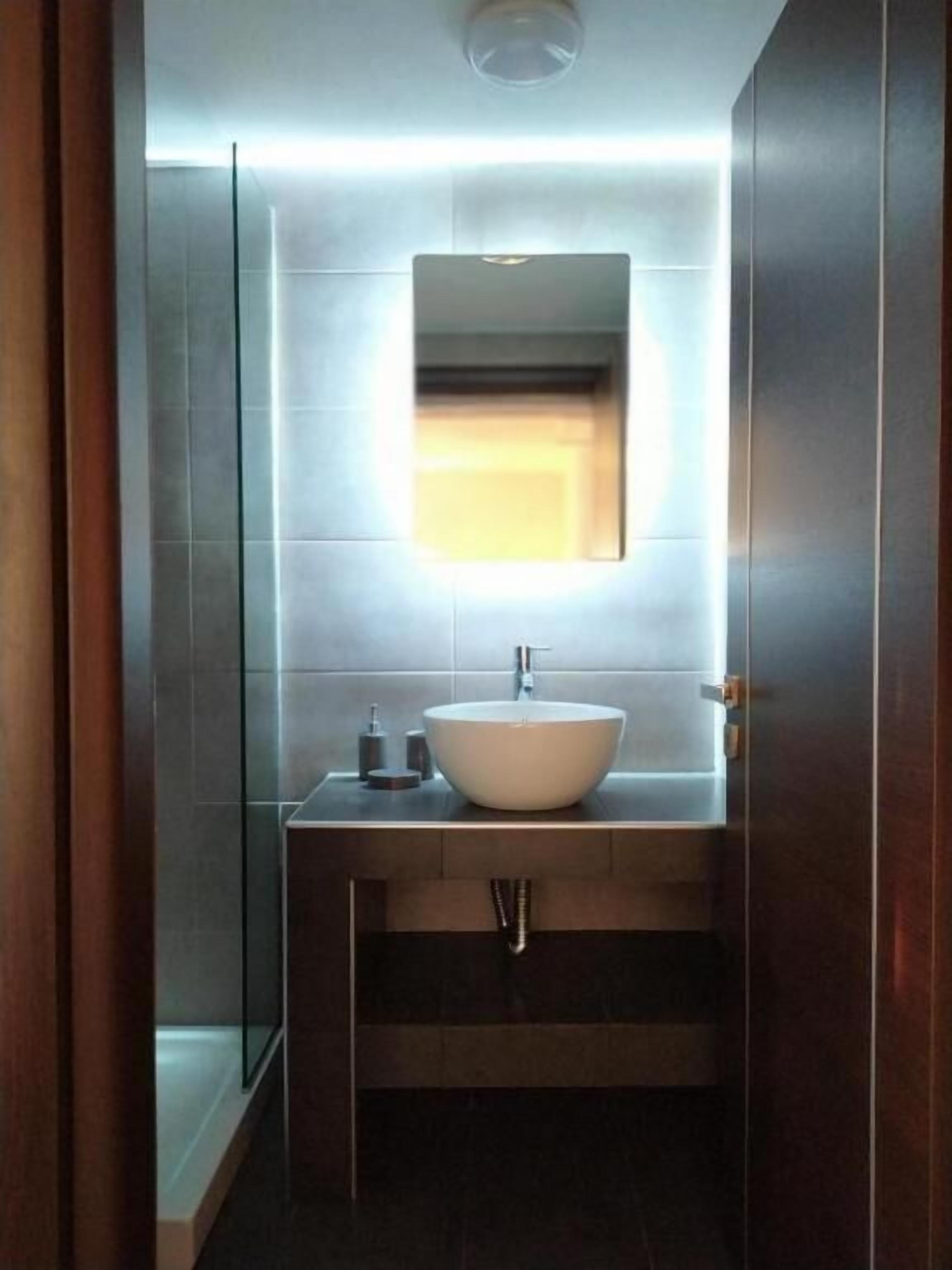 A modern bathroom with a large vessel sink, a mirror above it, and a shower area to the left.
