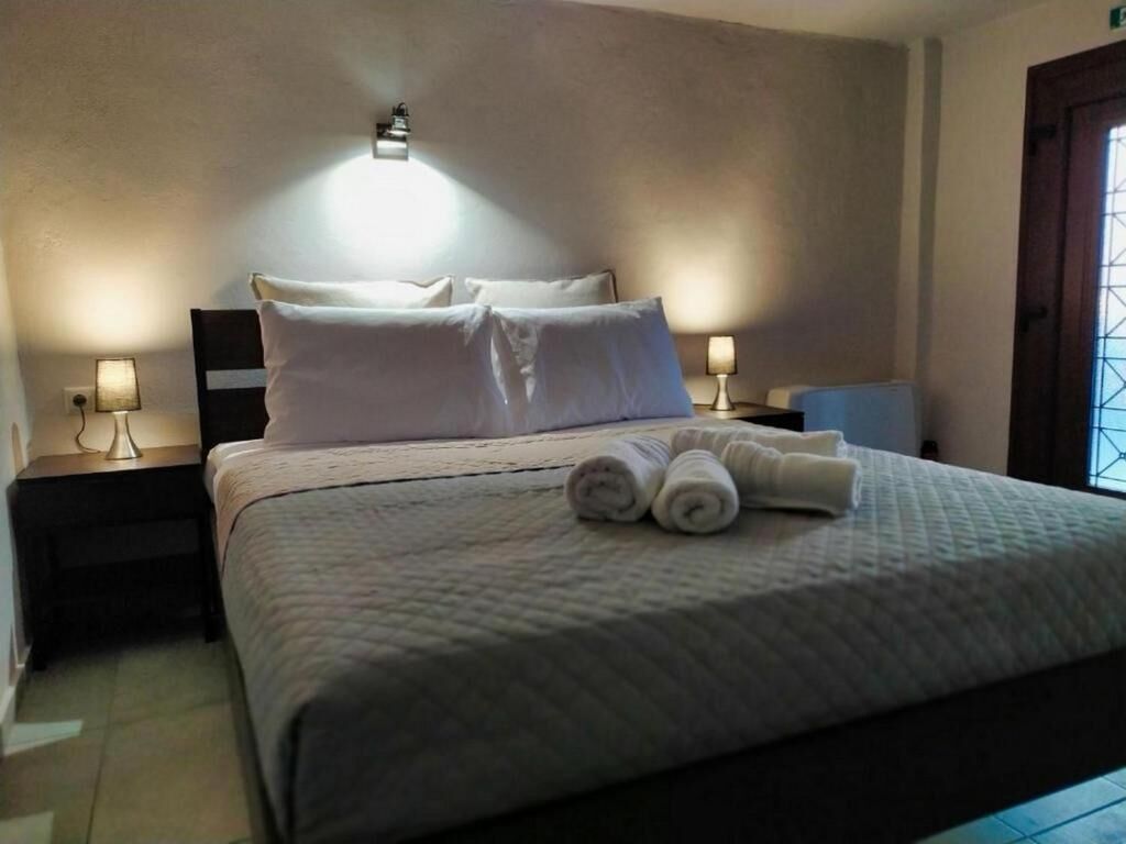A neatly made bed with white linens and rolled towels, two bedside lamps, and a window with a view.