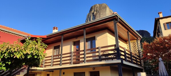 Un bâtiment à deux étages doté d’un balcon, d’une cheminée et d’une grande formation rocheuse en arrière-plan.