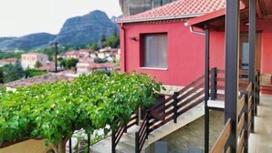 Un edifici vermell amb una escala que condueix a un balcó, envoltat de vegetació i muntanyes al fons.