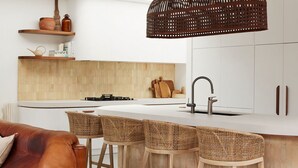 Una cucina moderna con isola centrale, sgabelli da bar, lampada a sospensione e pannello di legno a rivestimento.