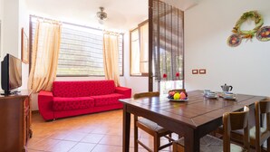 A room with a red sofa, wooden dining table, chairs, a TV on a cabinet, and a window with curtains. - 2404 Villa Cieloazzurro - Bilo by Barbarhouse (Nardò)