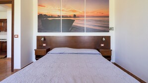 A bedroom with a large bed, wooden headboard, two bedside tables, and a wall-mounted painting of a sunset over water. - 2404 Villa Cieloazzurro - Bilo by Barbarhouse (Nardò)