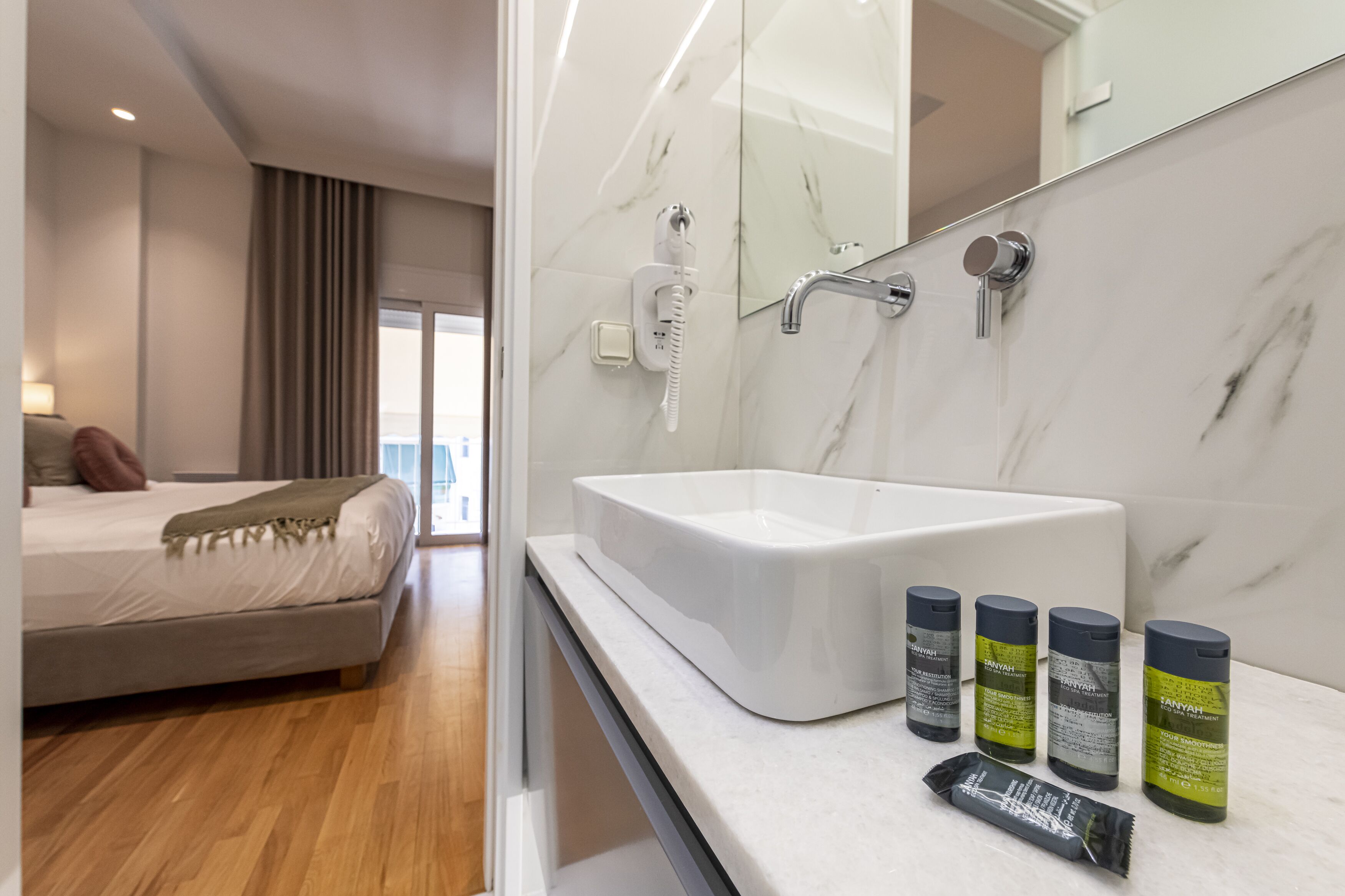 Une chambre d’hôtel moderne avec un grand lit, une salle de bain dotée d’un lavabo blanc et d’articles de toilette, ainsi qu’un grand miroir.