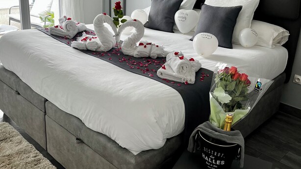 A modern hotel room with a large bed, grey upholstered headboard, white bedding, and a small bedside table with a bottle and a mug. - Casa PETRA SALGA (CORTE)