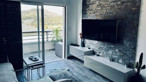 A modern living room with a large TV mounted on a stone wall, a sofa, a coffee table, and a balcony with a view of the mountains. - Casa PETRA SALGA (CORTE)