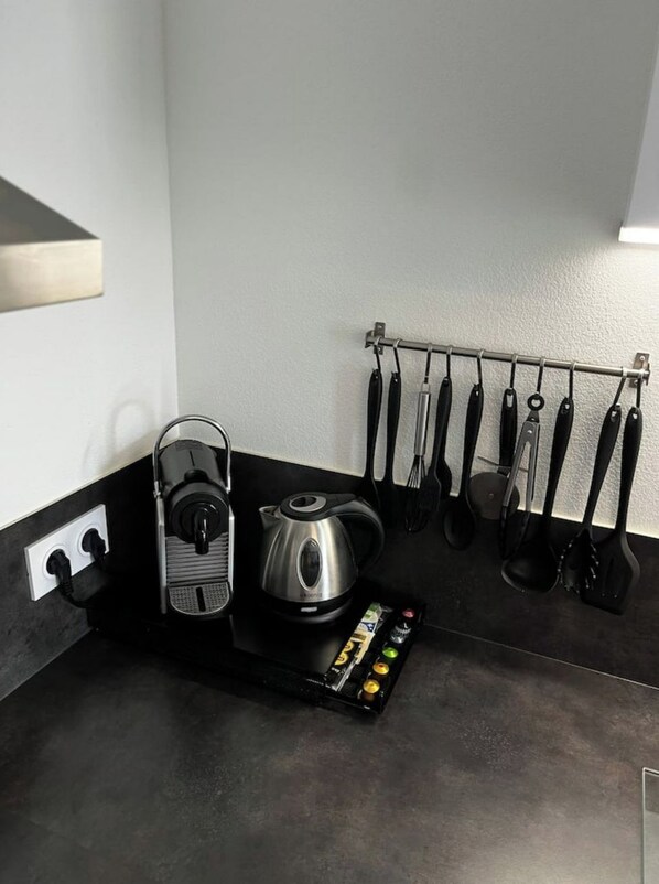 A kitchen with a coffee maker, kettle, and a rack holding various utensils.