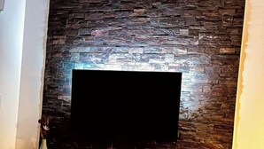 A modern living room with a stone wall and a flat-screen TV mounted on it. - Casa PETRA SALGA (CORTE)