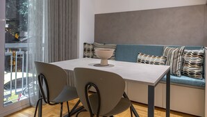 Un espace repas moderne avec une table et des chaises, un bol posé sur la table, et un canapé agrémenté de coussins à motifs.