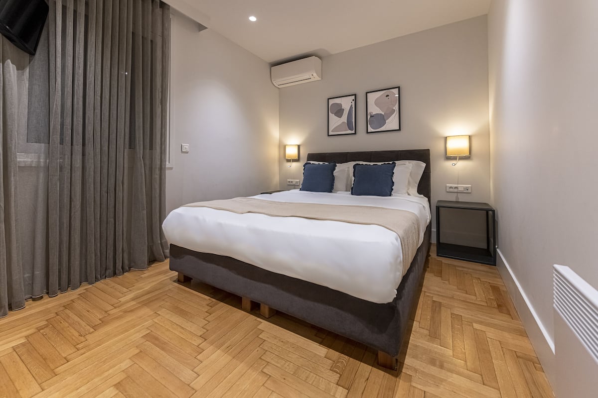 A modern hotel room with a large bed, wooden flooring, and two bedside lamps.