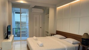 Una habitación de hotel con cama, televisor, lámpara de noche y vistas al balcón exterior.