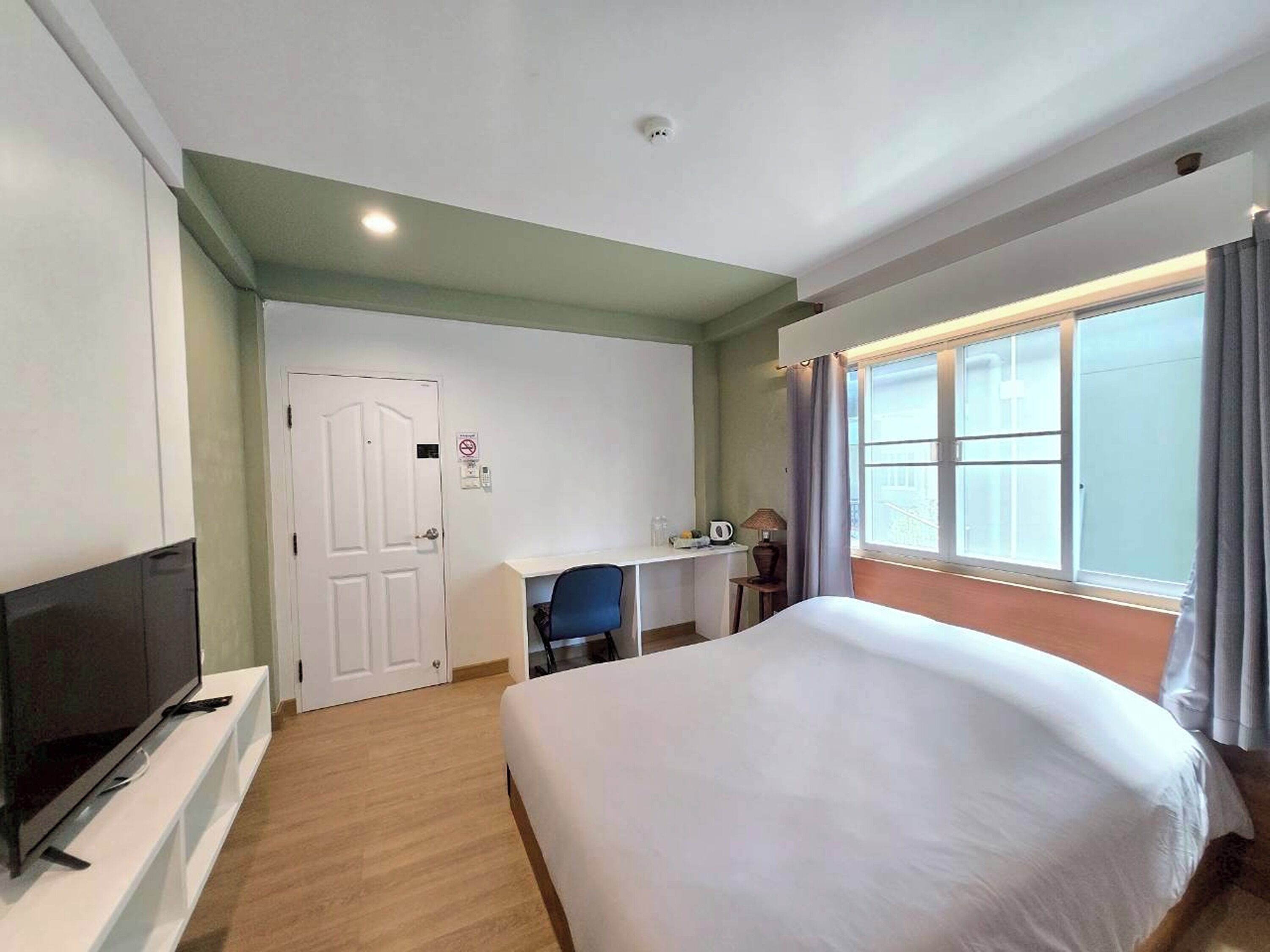 A hotel room with a bed, a desk, a television, and a window with curtains.