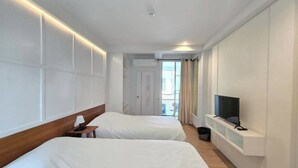 Habitación de hotel con dos camas, un televisor, una mesita con una lámpara y una ventana con cortinas.