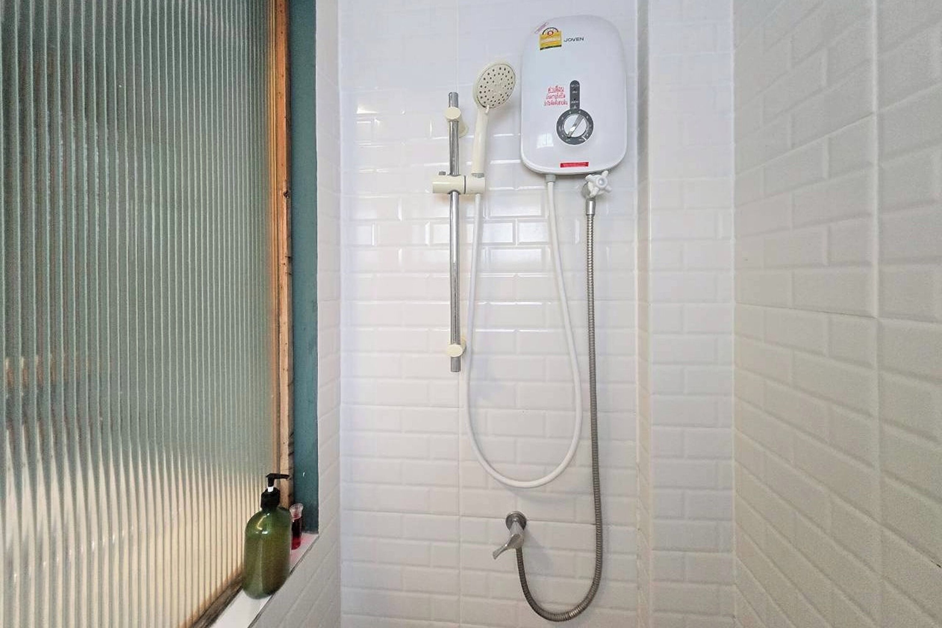 A bathroom with a white tiled wall, a shower with a handheld showerhead, a handheld shower attachment, and a handheld shower hose.