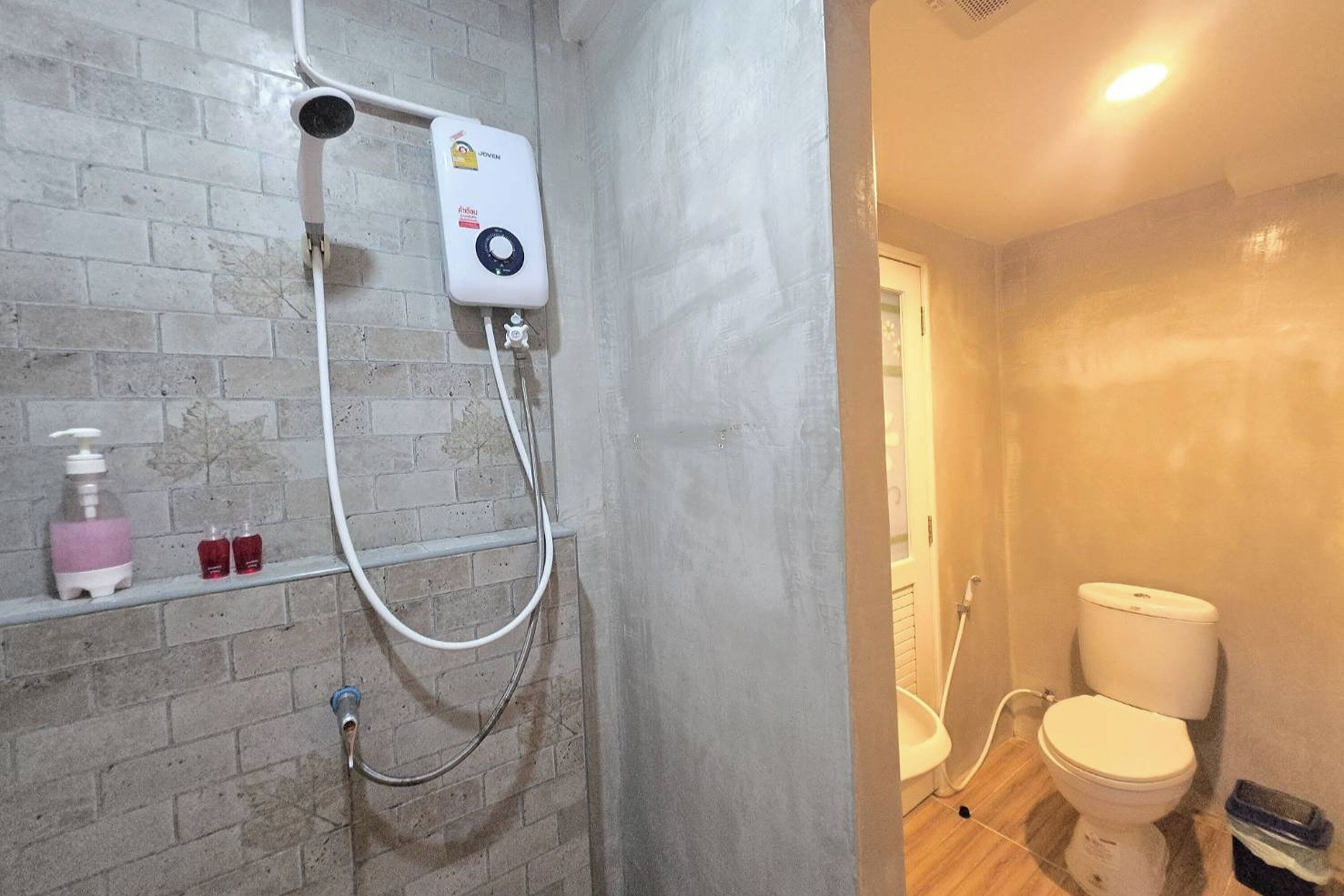A bathroom with a shower, toilet, and a shelf with toiletries.