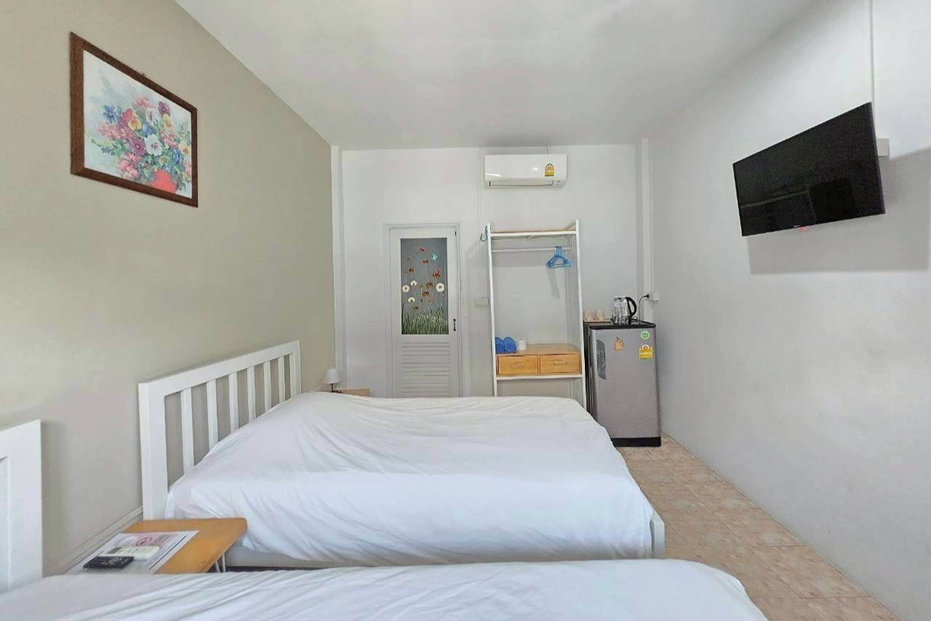 A hotel room with two beds, a TV, a small kitchenette, and a door leading to a bathroom.