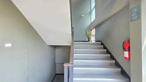 Una escalera con un extintor en la pared, una planta en el rellano y un cartel que indica el número de habitación 2.