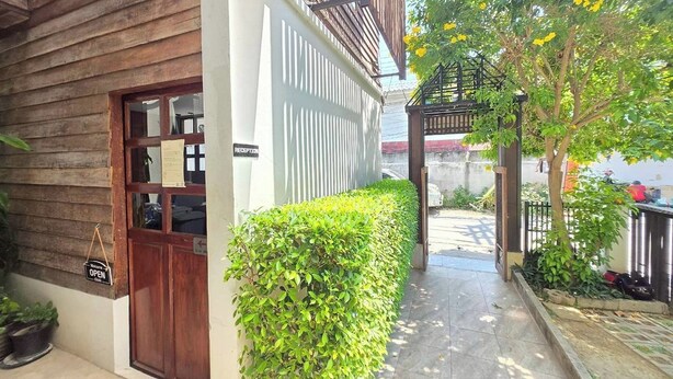 Un edificio de madera con recepción, un sendero pavimentado y un pequeño jardín con un árbol y flores amarillas.