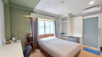 A hotel room with a bed, a desk with a chair, a wardrobe, and an air conditioning unit.