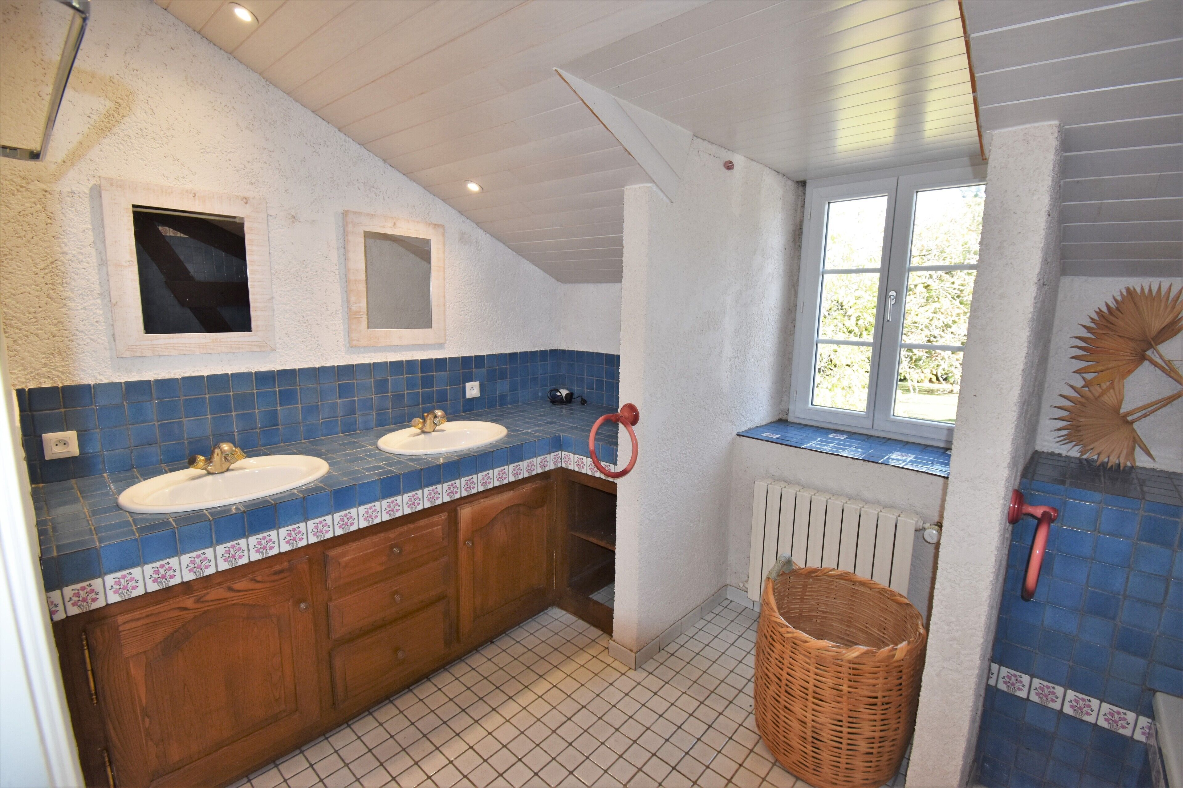 Une salle de bain avec deux lavabos, des meubles en bois, une fenêtre et un radiateur.
