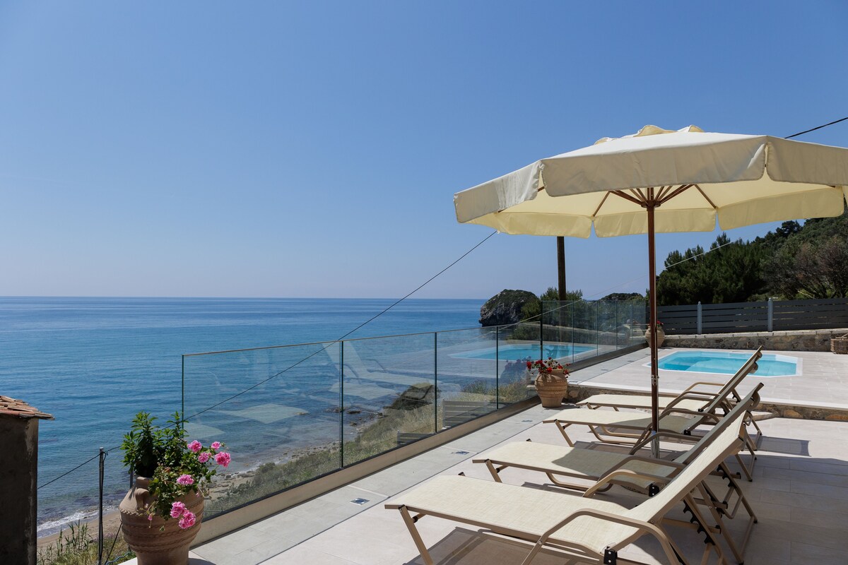 A balcony with a glass railing overlooking a pool and the sea.
