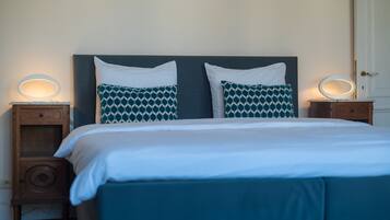 Cama bem arrumada com esquema de cores branco e azul, com duas mesas de cabeceira com luminárias.