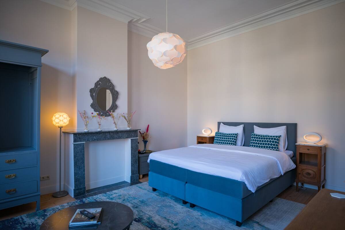 A bedroom with a bed, bedside tables, a dresser, and a hanging light fixture.