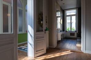 A hallway with wooden flooring, white doors, and a view of a cityscape through large windows. - Garden of Eden (Antwerp)