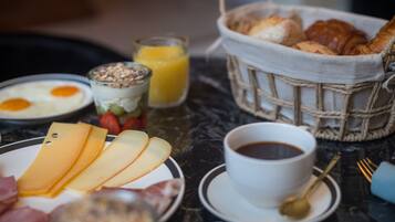 A breakfast table with cheese, eggs, yogurt, fruit, croissants, and coffee.