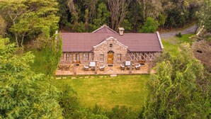Un bâtiment en pierre avec un toit rouge, entouré de verdure et doté d’une terrasse dallée avec des meubles d’extérieur.