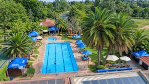 A swimming pool surrounded by palm trees and sun loungers, with a view of a residential area in the background. - The Residences at Karen Country Club (Nairobi)