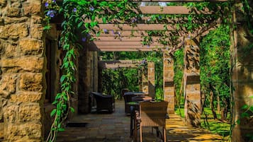Eine Terrasse mit Steinmauern, Korbmöbeln und einer mit Grünpflanzen bewachsenen Pergola.
