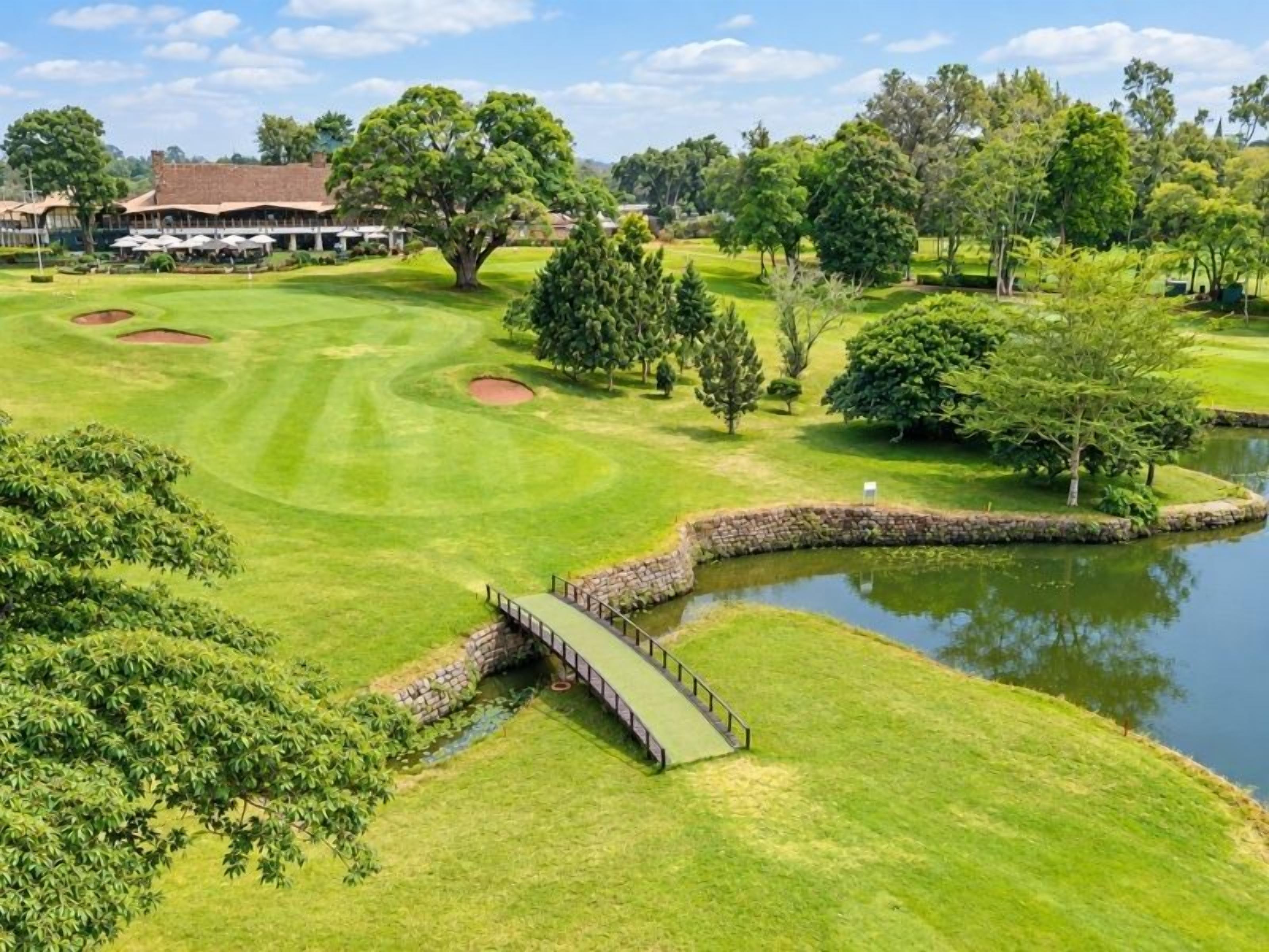 A golf course with a pond, a bridge, and a building in the background.