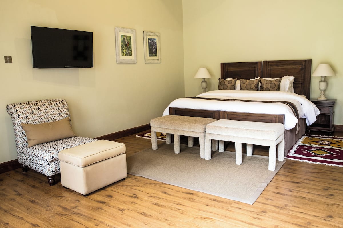 Une chambre à coucher avec un lit, deux tables de chevet, un téléviseur fixé au mur et un fauteuil à motifs.
