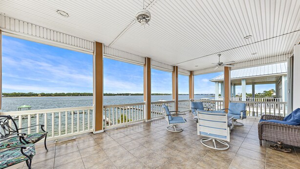 Un espace extérieur abrité avec vue sur un lac, comprenant un coin salon avec des chaises et une table, ainsi qu’une structure couverte dotée d’une rambarde.