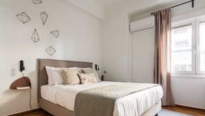 Un dormitorio ordenado con cama, mesita de noche, aire acondicionado de pared y ventana con cortinas.