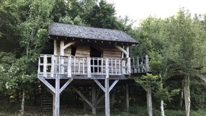 A wooden treehouse with a balcony, surrounded by trees. - Charming tree house in Normandy (Essay)