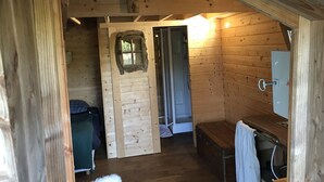 A wooden cabin with a lofted sleeping area, a small bathroom with a wooden door, and a bench. - Charming tree house in Normandy (Essay)