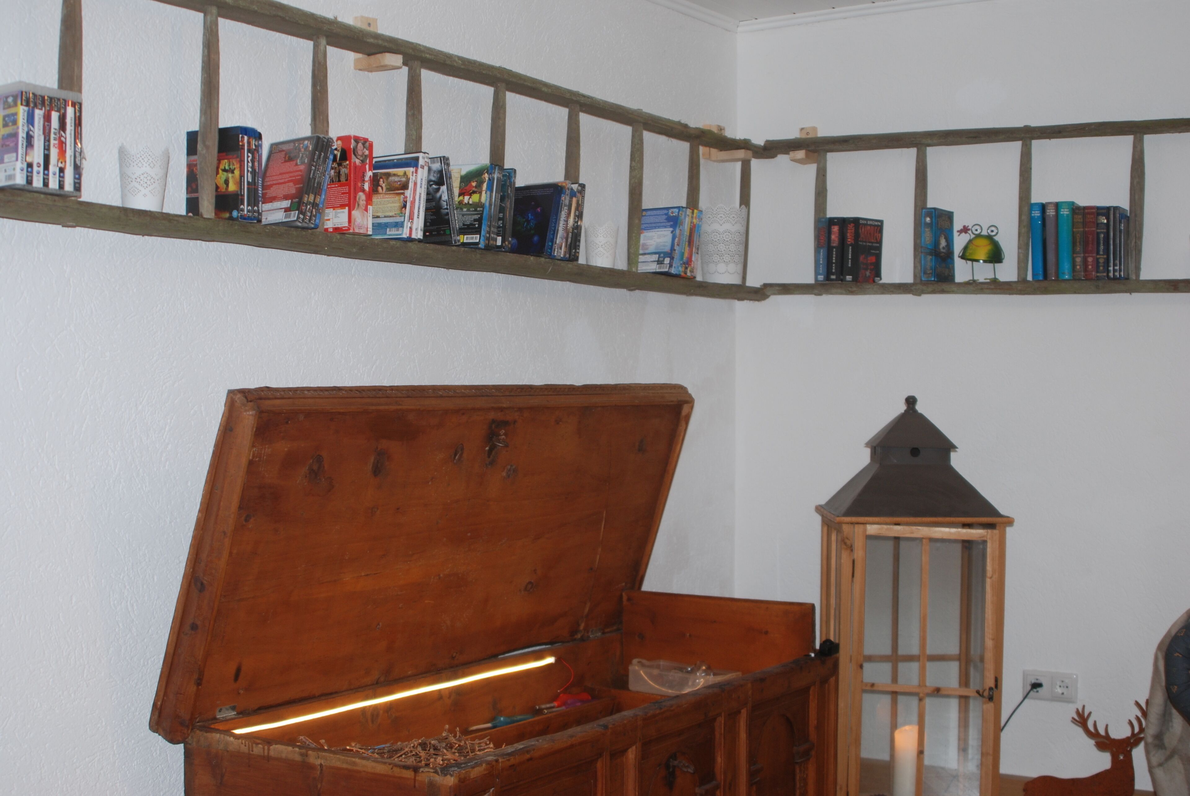A wooden chest with a hinged lid, a shelf with books and a lantern, and a wall socket.