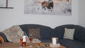 Un salón acogedor con un sofá azul estampado, una mesa de centro de madera con una botella de vino, copas y una vela.