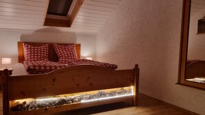 Un dormitorio con una cama de madera, ropa de cama a cuadros, una mesita de noche, una lámpara y un arreglo decorativo de piñas.